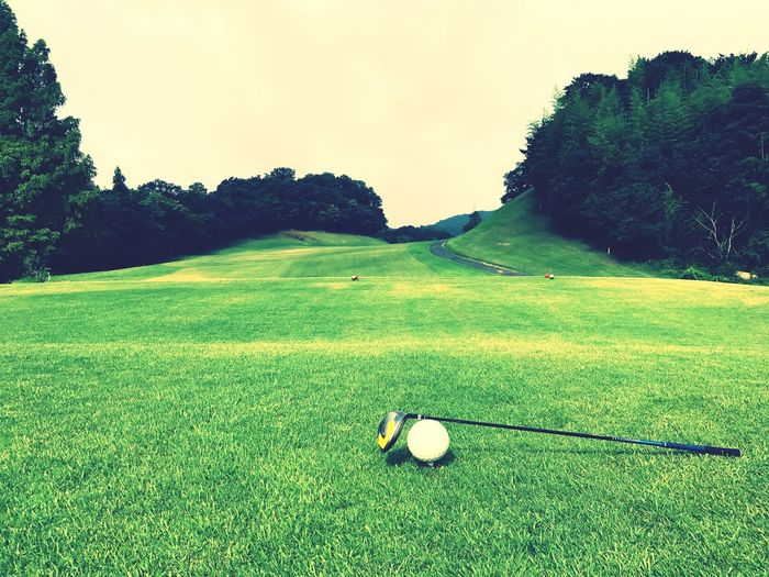 Golf ball and cue on grassy field against sky