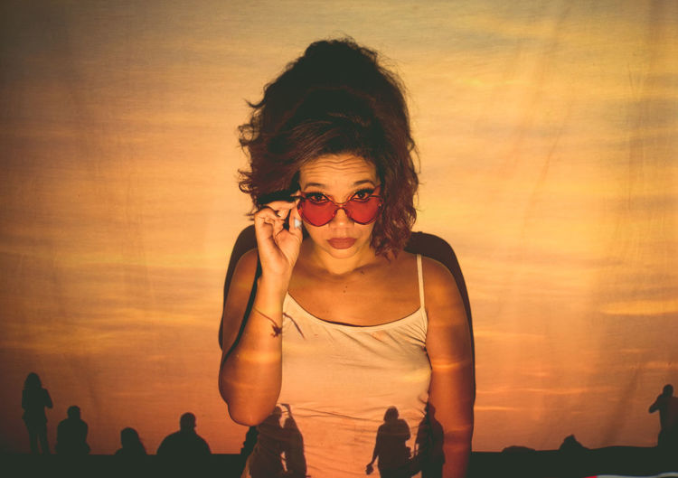 Portrait of woman wearing sunglasses standing against orange backdrop