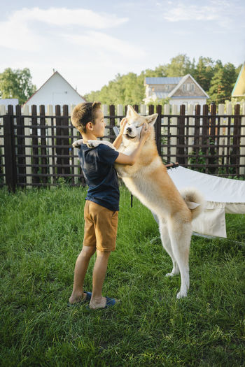 Boy playing with akita dog on grass at backyard