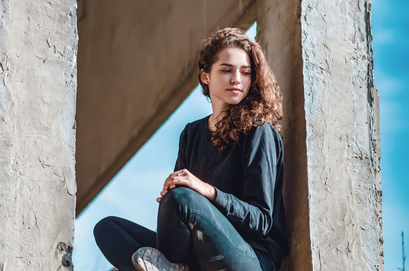 Curly cute young woman sitting in window of unfinished house. architecture, construction.