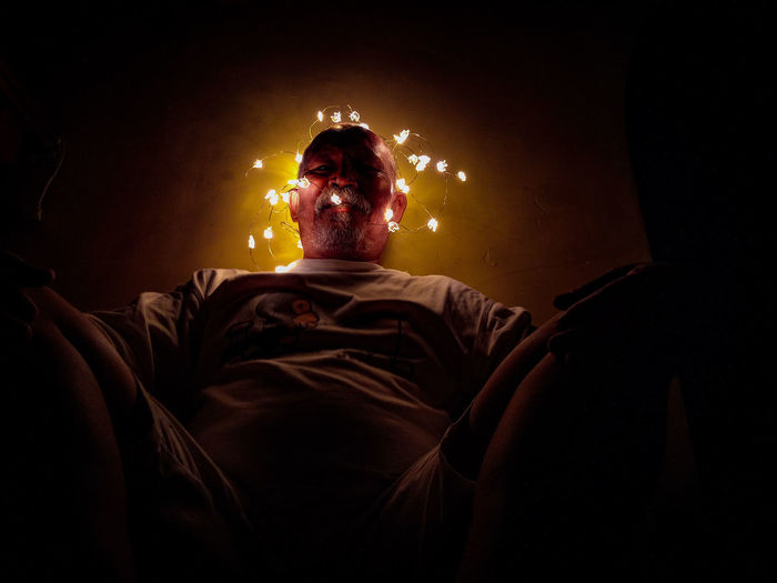 Low angle view of man sitting amidst illuminated string lights against wall