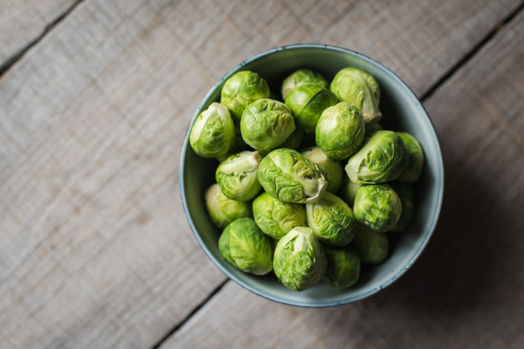 Overhead view of bowl of brussels sprouts on wooden background.