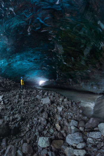 Tourist in outerwear standing near uneven holes in ice surface while exploring cave in vatnajokull glacier on winter day in iceland