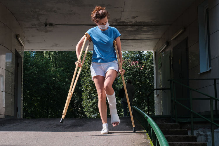 A woman with a broken leg walks down a ramp using orthopedic crutches.