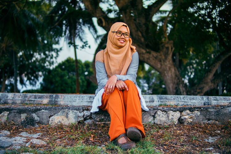 A portrait of a muslim woman smiling and sitting on a bench at park with flare