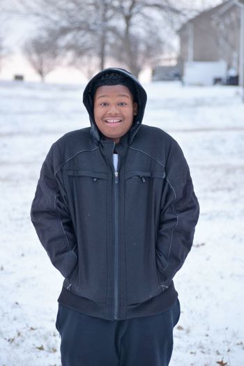 Portrait of smiling man with hands in pockets while standing on snow
