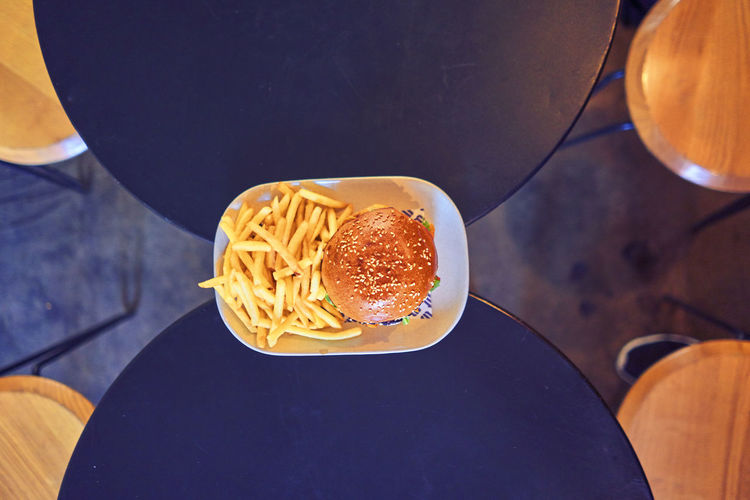 Directly above shot of burger and french fries in plate on tables at restaurant