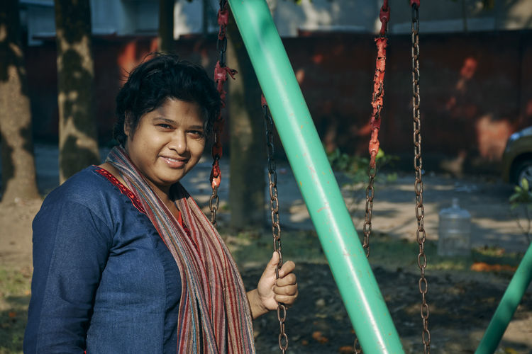 Casual looking fashionable indian woman leisurely spending time in public park, standing near swing