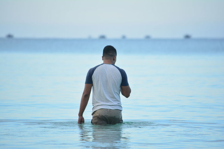 Rear view of man wading in sea against sky