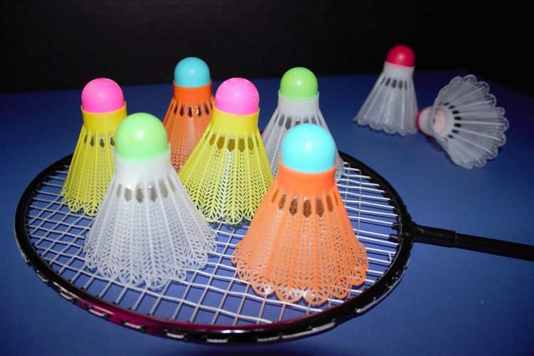 High angle view of multi colored shuttlecocks and rackets on table against black background