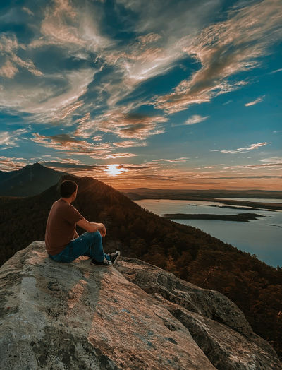 Man sitting on rock looking at view of sky