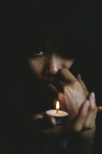 Close-up portrait of woman holding lit tea light against black background