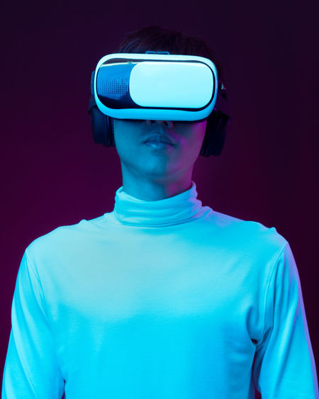 Young man using virtual reality simulator against colored background