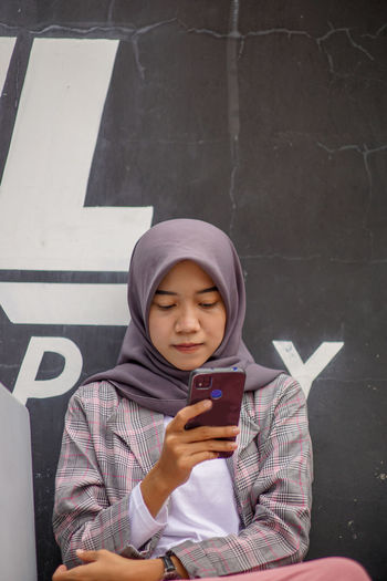 Muslim woman wearing modern hijab sitting and playing social media in cafe