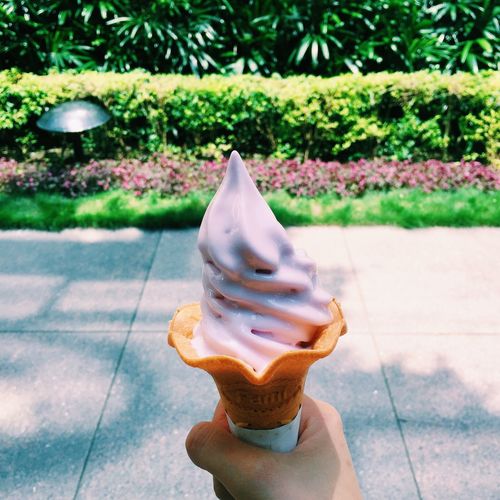 Cropped image of hand holding strawberry ice cream on sidewalk