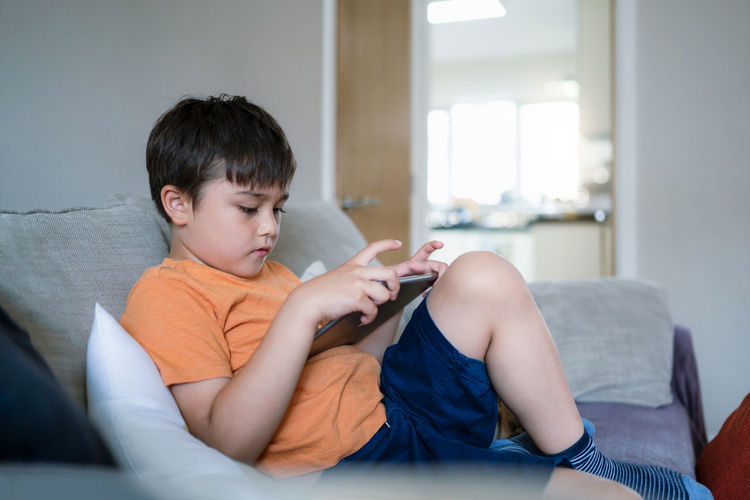 Rear view of boy using mobile phone at home
