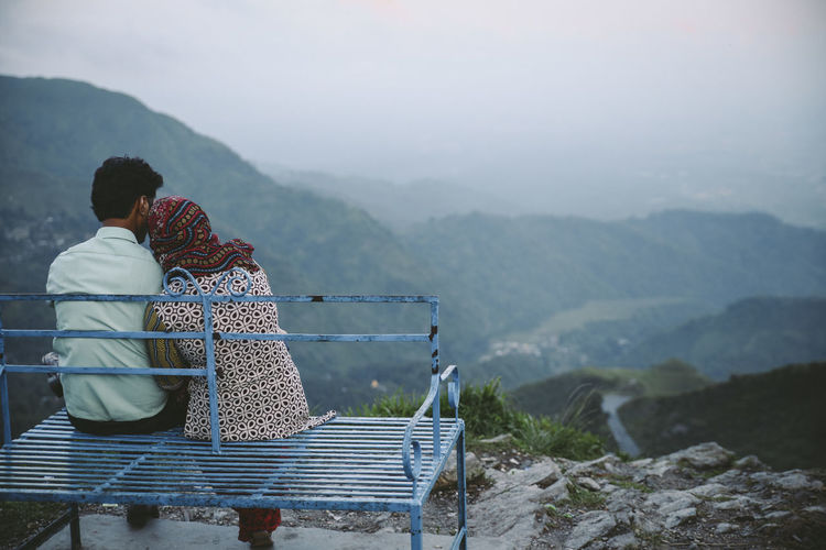 Rear view of couple sitting on seat against mountains