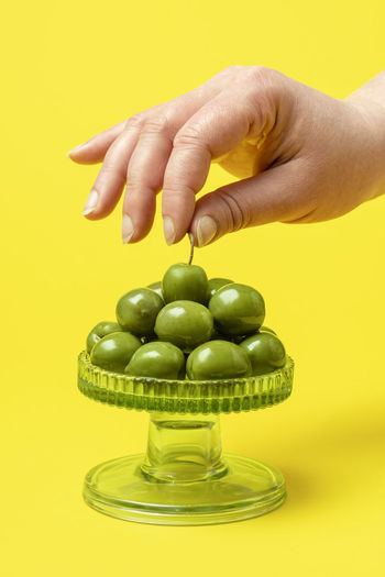 Close-up of hand holding fruit against yellow background