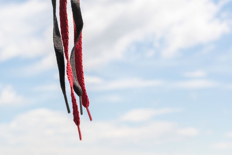 Many colored shoelaces, hanging on a background of sky and clouds, pointed down