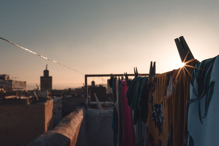 Clothes drying on clothesline by building against sky at sunset