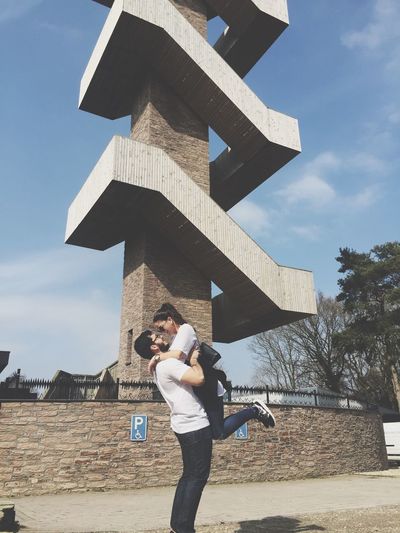 Man carrying woman standing against built structure in city