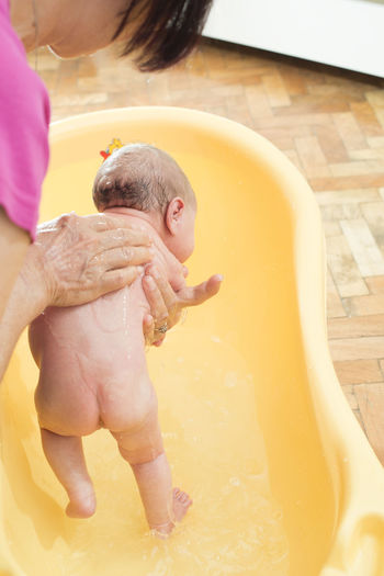 High angle view of grandmother bathing shirtless baby girl in bathtub at home