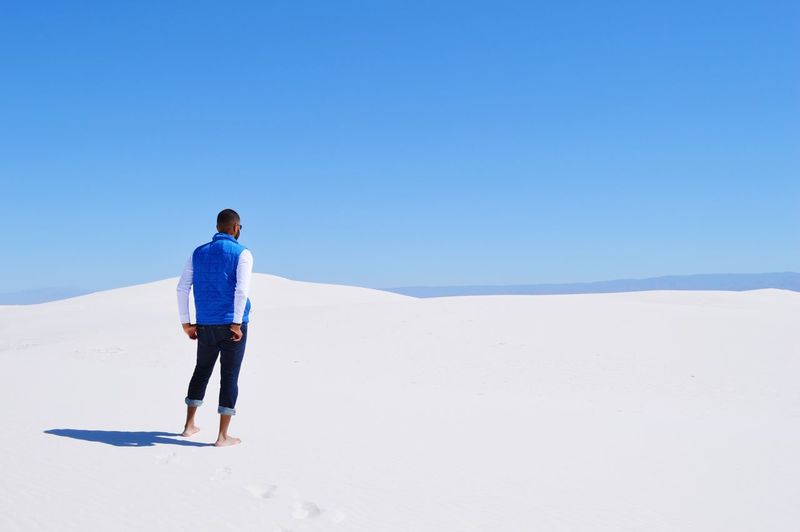 Rear view of man standing on sand dune against clear sky