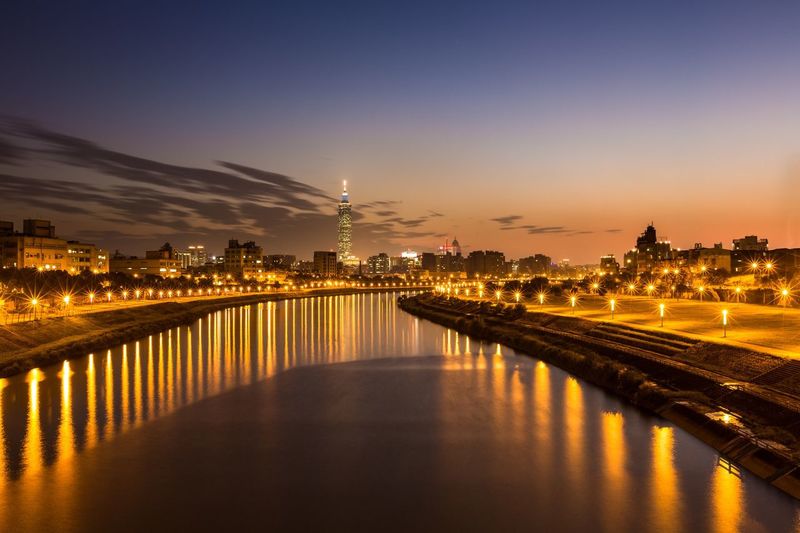 Canal amidst illuminated lighting equipment against sky at dusk