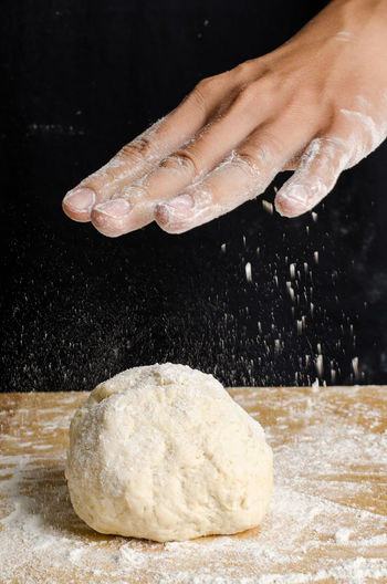 Cropped hand with dough at table against black background