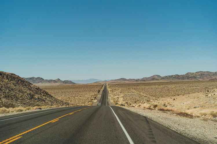Road passing through desert against clear sky
