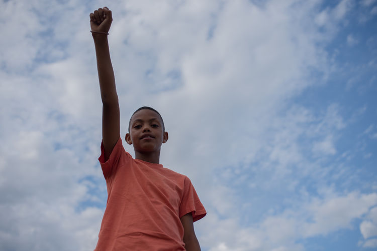 Low angle view of boy with arms raised against sky