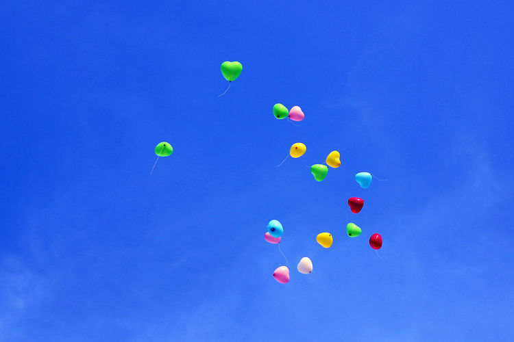 Low angle view of colorful helium balloons against sky
