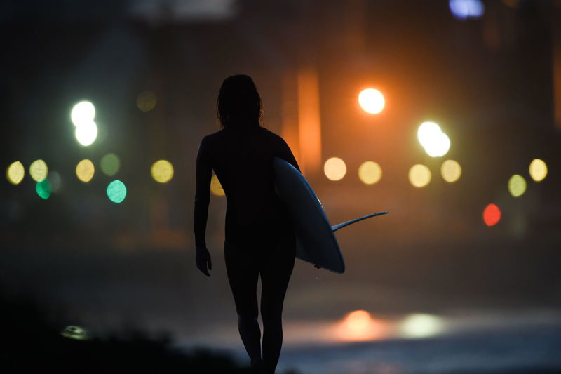 Rear view of silhouette woman with surfboard at beach during night