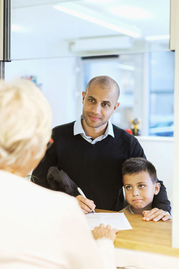 Father and son looking at receptionist while filling forms in orthopedic clinic