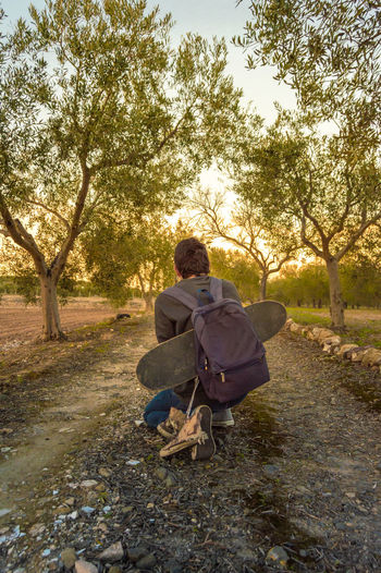 Rear view of man sitting on road against trees