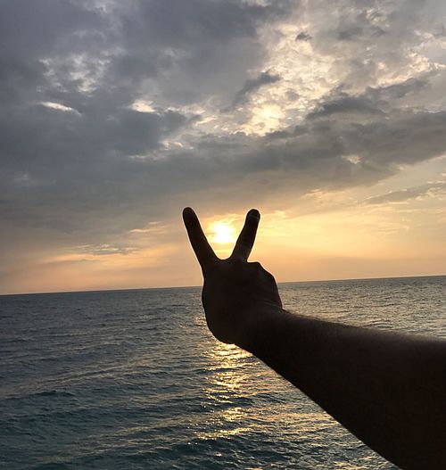 Person hand on sea against sky during sunset