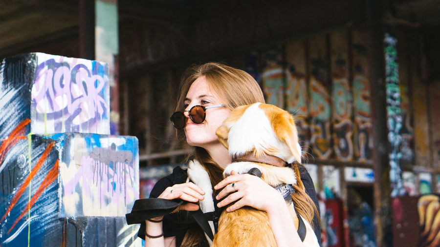 Woman wearing sunglasses while holding dog against graffiti wall