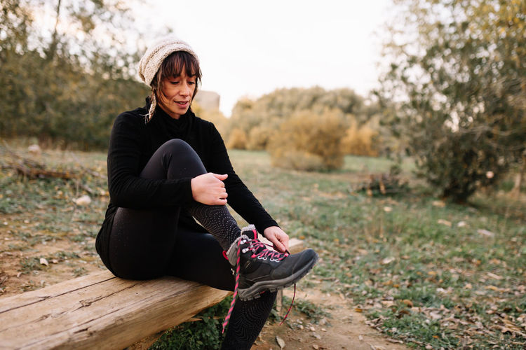Smiling woman wearing knit hat tying shoelace at park