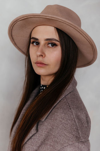 Woman in beige cashmere coat and beige hat against the background of a white wall  close up