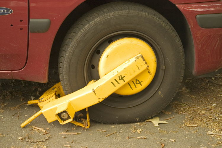 Close up of a car blocked by a yellow wheel clamp.