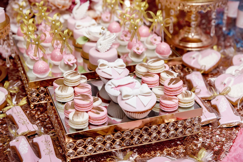 Pink cupcakes, cakes and macarons at a candy bar, decorated with caramel bows and swans