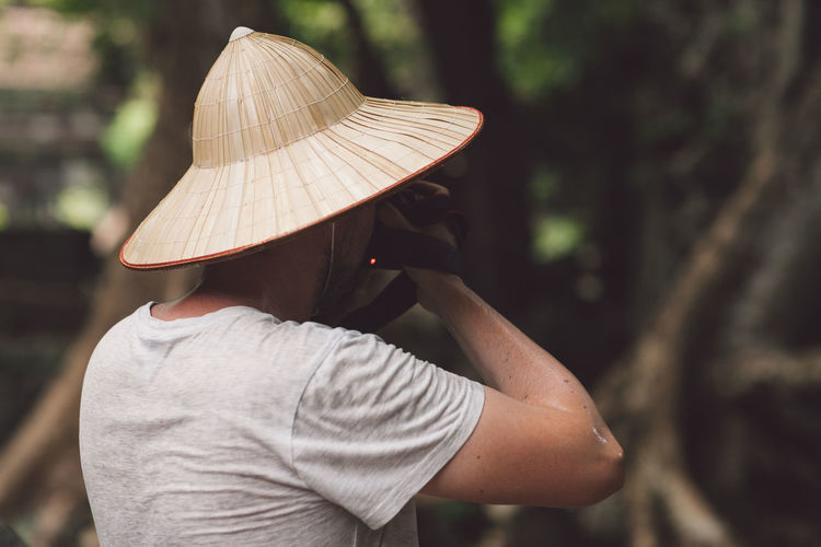 Rear view of man wearing hat photographing forest