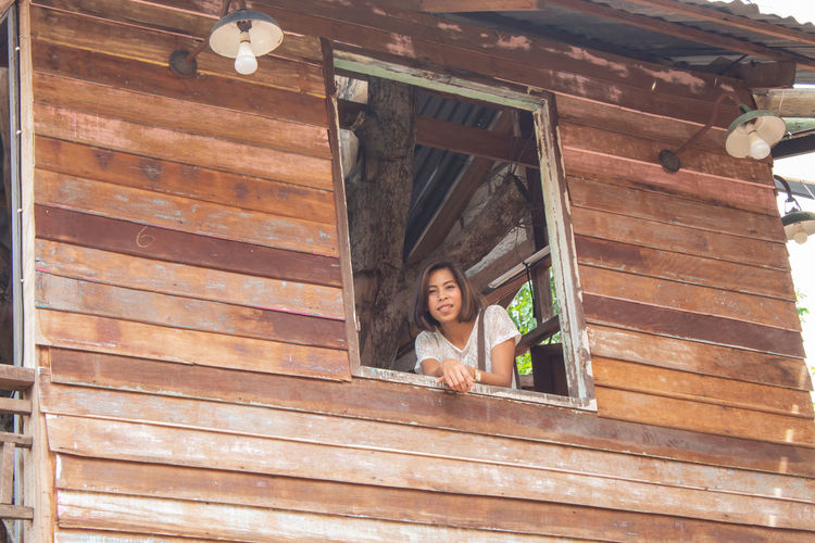 Low angle view of smiling woman looking through window from log cabin