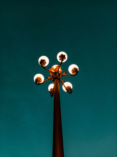 Low angle view of illuminated lighting equipment against clear blue sky