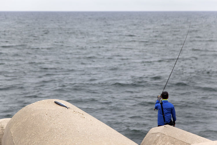 Rear view of woman standing on rock while fishing at sea