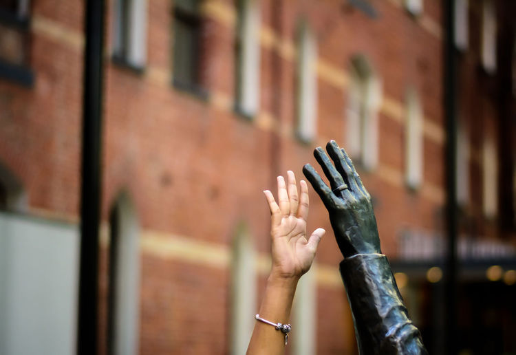Cropped hand of person by statue against building