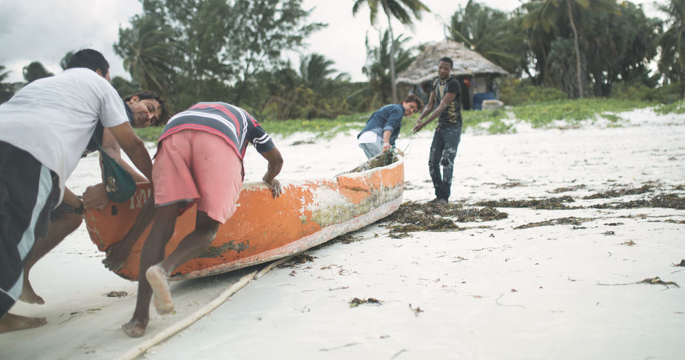 A group of people pulling a wooden boat by a rope on a sand beach.