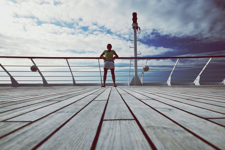 Full length of woman standing on boat deck against cloudy sky