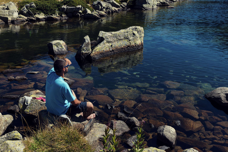 High angle view of man sitting on rock by lake