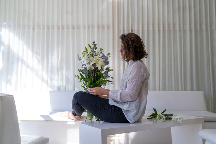 Side view of woman sitting by potted plant